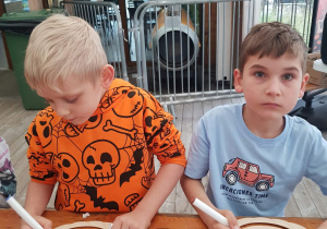 Dzieci ozdabiają dynię ze sklejki.