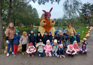 Dzieci stoją przy wiewiórce z wychowawcami.