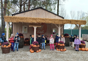 Dziecistoją na tle domku z dyniami.
