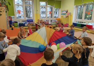 Dzieci bawia się chustą animacyjną na której są kolorowe balony