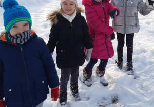 Na pierwszym planie widać od lewej chłopca i 3 dziewczynki a za nimi drzewa pokryte śniegiem