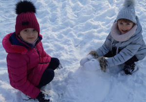 Na śniegu kucają dwie dziewczynki, dotykają śniegu