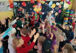 Dzieci przebrane na bal karnawałowy tańczą z bańkami mydlanymi