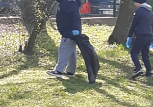 Dwóch chłopców spaceruje po ogrodzie, jeden chłopiec trzyma worek na śmieci