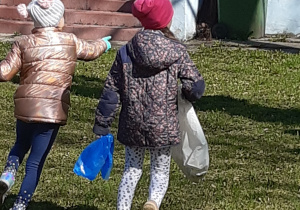 dwie dziewczynki trzymają w ręku worki i zbierają śmieci