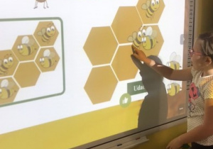 Dzidziewczynka rozwiązuje zadanie matematyczne na tablicy multimedialnej