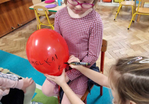Dzieci podpisują się jubilatce na balonie czerwonym