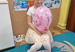 Jubilatka w koronie trzyma różowego balona z podpisami dzieci