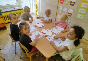Dzieci przy stoliku malują dłońmi szablon zająca