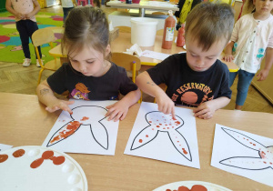 Dziewczynka i chłopiec malują dłońmi szablon zająca