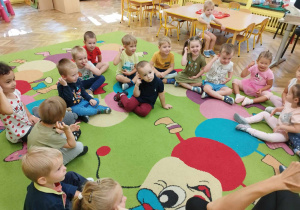 Dzieci siedzą w kole na dywanie z animatorem