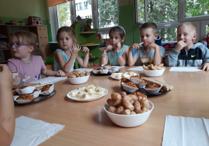 Dzieci siedzą przy stole i częstują się słodkościami urodzinowymi