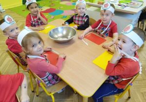 Dzieci w czerwonych koszulkach i fartuszkach siedzą przy stole