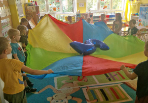 Dzieci unoszą kolorową chustę z balonem