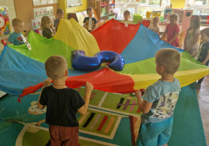 Dzieci unoszą kolorową chustę z balonem