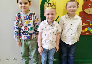 Trzech jubilatków w koronach stoi w przedszkolnej sali.