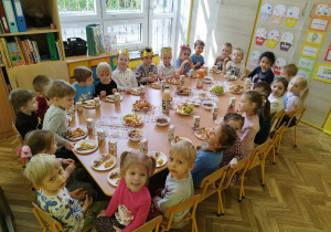 Dzieci jedzą urodzinowy poczęstunek przy stole.
