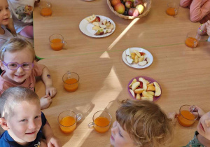 Dzieci siedzą przy stole na którym znajdują się obrane owoce i sok