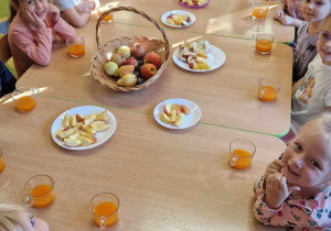 Dzieci siedzą przy stole na którym znajdują się obrane owoce i sok