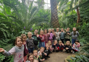 Dzieci pozują do zdjęcia grupowego na tle roślinności