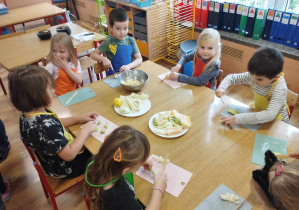 Dzieci siedzą przy stole i kroją owoce.