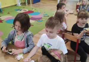 Dzieci siedzą przy stole i jedzą sałatkę.