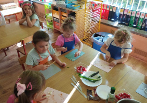 Dzieci siedzą przy stole i kroją składniki na sałatkę.