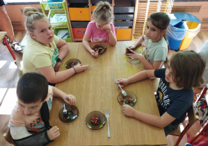 Dzieci jedzą własnoręcznie przygotowaną sałatkę.