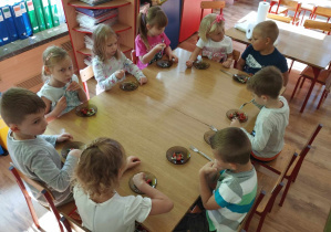 Dzieci siedzą przy stole i jedzą własnoręcznie przygotowaną sałatkę.