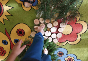 Na zdjęciu widać nogi dziecka, które chodzi po drewnianych krążkach.