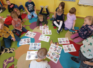 Dzieci siedzą na dywanie i dopasowują obrazki do kart.