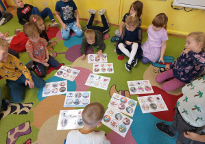 Dzieci siedzą na dywanie i dopasowują obrazki do kart.
