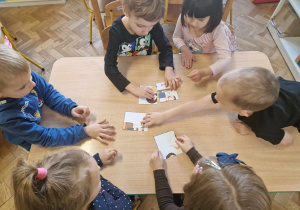 Grupa dzieci układa na stoliku puzzle z pociętych elementów
