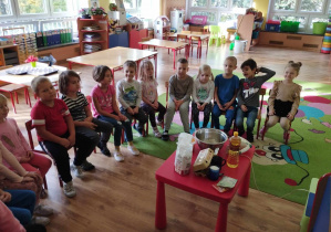 Dzieci siedzą wokół stolika, na którym widać składniki na babeczki.