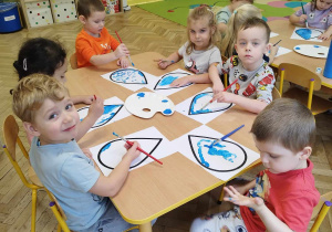 Dzieci malują niebieską farbą szablon przedstawiający kropelkę deszczu.
