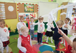 Dziewczynki i chłopcy tańczą z biał czerwonymi bibułami