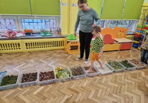 Chłopiec z pomocą nauczyciela idzie jesienną ścieżką sensoryczną