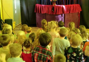 Dzieci oglądają przedstawienie teatralne. Na scenie widać kukiełkę przedstawiającą diabełka.