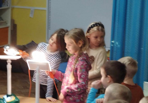 Dzieci oświetlają lampami panele fotowoltaiczne.