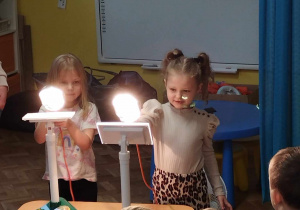Dziewczynki oświetlają lampami panele fotowoltaiczne.