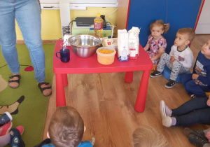 Dzieci siedzą dookoła stolika z produktami na babeczki dyniowe.