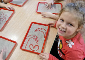 Dzieci rysują palcem na tacce z piaskiem