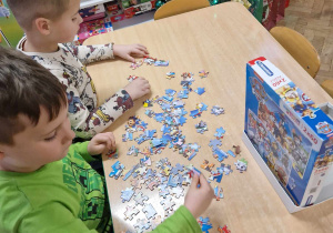 Chłopcy siedzą przy stole i układają puzzle