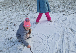 Dziewczynki rysują patykiem po śniegu