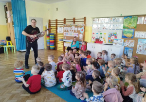 Dzieci oglądają mężczyznę grającego na gitarze elektrycznej.
