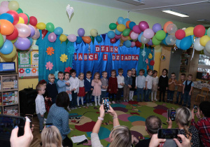 Dzieci ustawione w półkole śpiewają piosenkę.