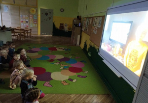 Dzieci oglądają film edukacyjny na tablicy multimedialnej.
