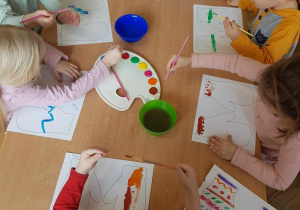 Dzieci malują farbami szablon rękawiczek.