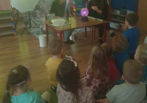 Dzieci uczestniczą w eksperymencie z kulą plazmową i świetlówką.