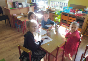 Dzieci siedzą przy stole i kolorują misie.